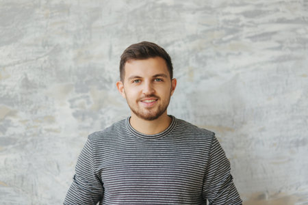 Handsome man with beard stand on the gray background in studio. He smile to camera