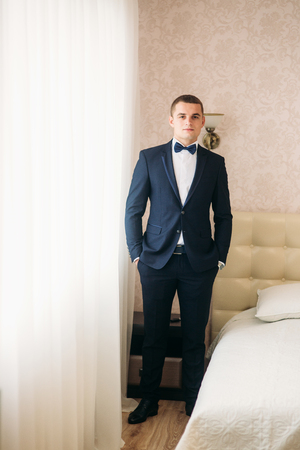 Handsome groom on a wedding day stand near the windowの写真素材