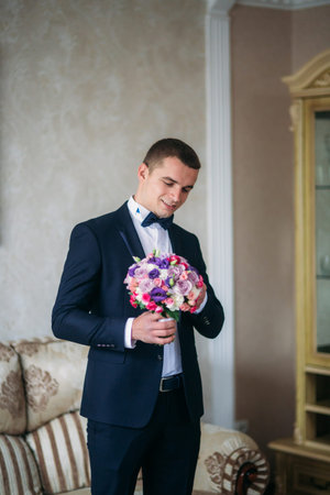 Handsome man in wedding suit hold a bouquet of flowersの写真素材