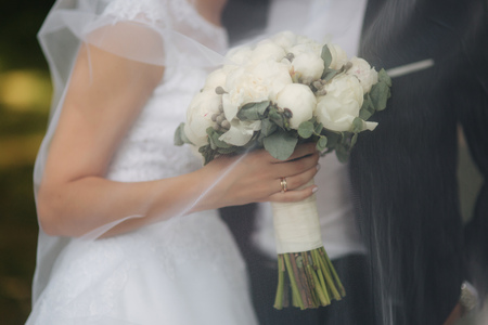 Young bride in beautiful white wedding dress stand near the wall. She hold a bouquet of flowers in handsの写真素材