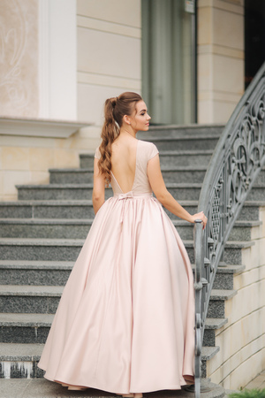 Elegant brunette stand on stairs by the hotel. Fashion model in evening dressの写真素材