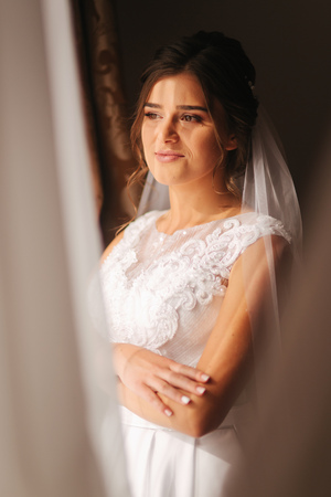Beautiful bride stand by the window. Morning with sunlights.の写真素材