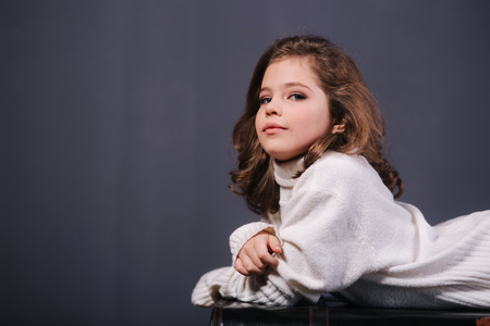 Little beautiful girl with brown hair in a white sweater. Studio. A princess poses for a photographer. Makeup and hairstyleの写真素材