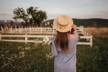 Back view of Beautiful lady. She hold a bouquet of flowers and smile. Background of farmの写真素材