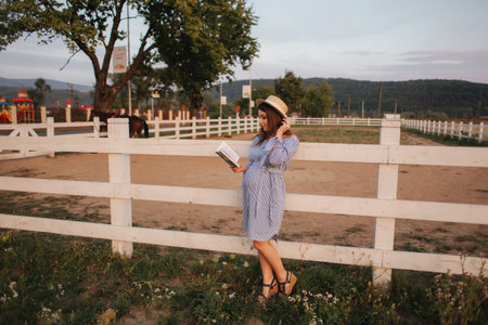 Beautiful pregnant woman read the book on the farm. She stand by the fance and look in to the book. Relaxの写真素材