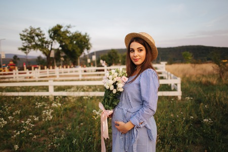 Back view of pregnant woman. She hold a bouquet of flowers and smileの写真素材