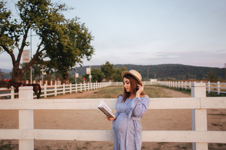 Beautiful pregnant woman read the book on the farm. She stand by the fance and look in to the book. Relaxの写真素材