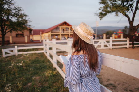 Back view of Beautiful pregnant woman read the book on the farm. She stand by the fance and look in to the book. Relaxの写真素材