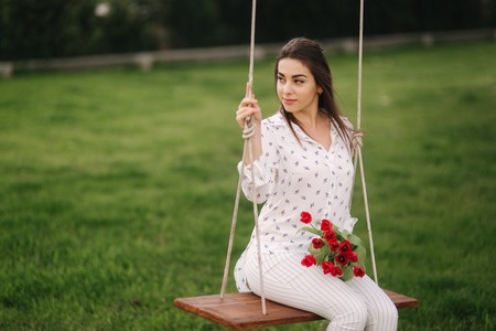 Lady in white sit on swing on the back yard of her house. She hold a re flowersの写真素材