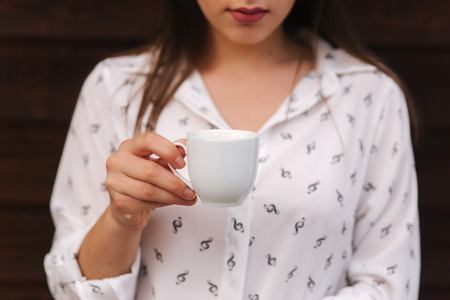 Beautiful girl hold a cup of coffee. White shirt. Wooden backgroundの写真素材