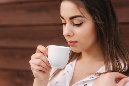 Beautiful girl hold a cup of coffee. White shirt. Wooden backgroundの写真素材