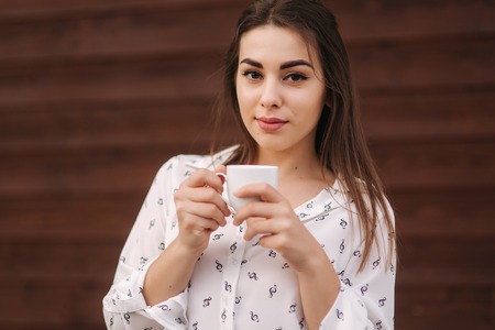 Beautiful girl hold a cup of coffee. White shirt. Wooden backgroundの写真素材