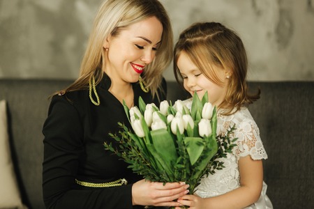 Little daughter give to mother bouquet of flowers. Mom and daughter at home. Bouquet of flowers on 8th of marchの写真素材