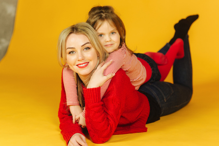 Little daughter five year old with her young mom. Little girl lay on my mothers back. Yellow backgroundの写真素材