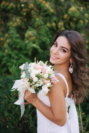 Gorgeous female in white dress slime. Beautiful girl hold a bouquet of flowers in hands