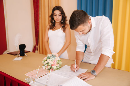 Groom and bride standing inside marriage house and sign the paper. Beautiful couple in white