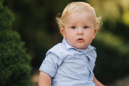 Happy little boy sit outside in summer time. Boy with curly blond hairの写真素材