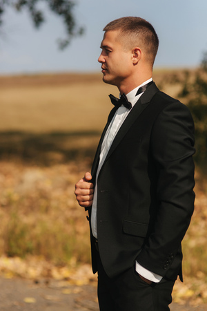 Young groom in suit otside. Handsome man in black suit. Model walking in the parkの写真素材