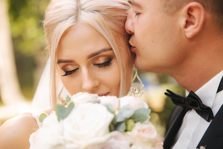 Closeup of groom kissing bride. Blond hair woman with bouquetの写真素材