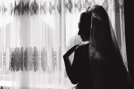 Silhouette of beautiful bride at home. Woman stand by the window in wedding dress. Black and whiteの写真素材
