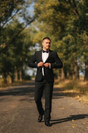 Young groom in suit otside. Handsome man in black suit. Model walking in the parkの写真素材