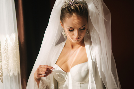 Portrait of beautiful bride at home. Woman stand by the window in wedding dress.の写真素材