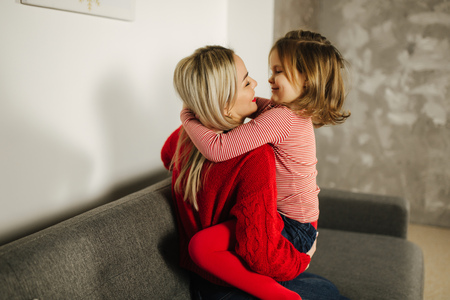 Little girl in red tights with mom in red sweater. Happy family at home. Daughter hug her motherの写真素材