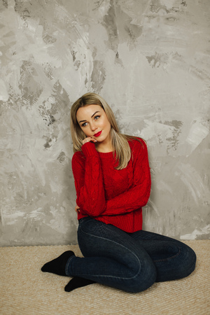 Beautiful woman in red sweater and red lips at home. Happy blond hair ladyの写真素材
