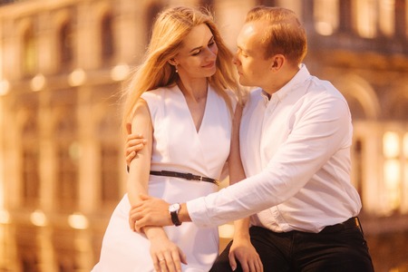 Wife and husband sist on the border in front of bilding with lights. Evening in the city. Night lightsの写真素材