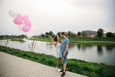 Young happy couple in love outdoors. Handsome man and beautiful woman on a walk in a spring blooming park. They keep helium ballsの写真素材