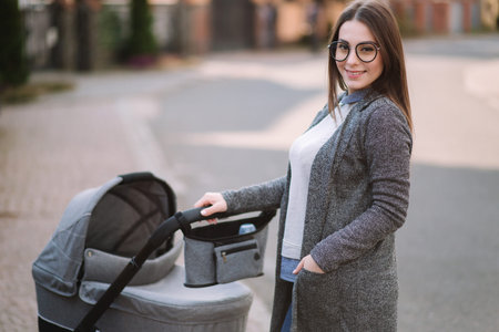 Family, child and parenthood concept - Happy mother with stroller in the park. Mom with sunglasses...