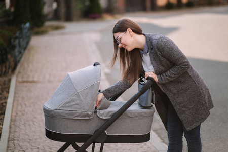 Young mom walking with daughter in stroller. Mother cares for the baby. Mom look in to the stroller and help baby to sleepの写真素材