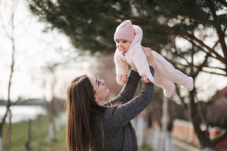 Side view of happy young mother holding babi girl in her hands and looking at her with love