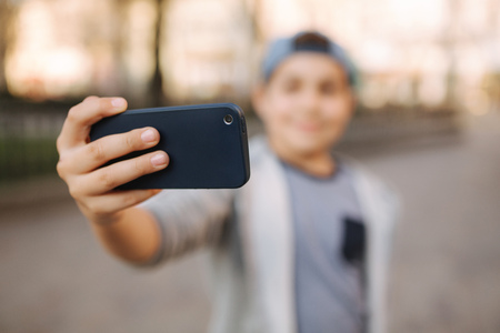 Young boy make a selfie on smartphone in the centre of the city. Cute boy in blue hat. Stylish school boy