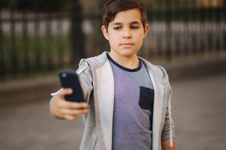 Young boy make a selfie on smartphone in the centre of the city. Cute boy in blue hat. Stylish school boyの写真素材