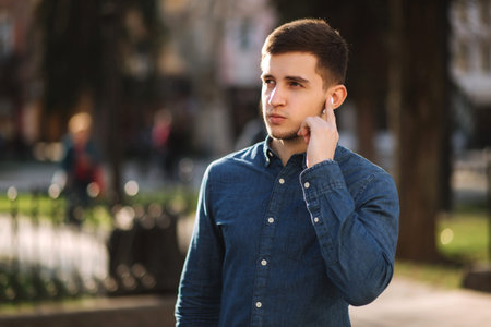 Handsome man put his finger on wireless headphones and speaks. Portrait of man makes conversation by the phoneの写真素材