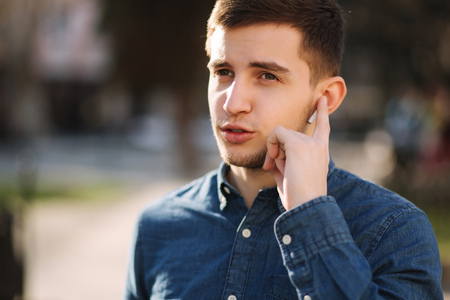 Handsome man put his finger on wireless headphones and speaks. Portrait of man makes conversation by the phoneの写真素材