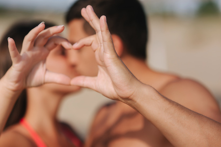 Happy young couple kiss and make a heart by hands. Couple walking on the beach. Loveの写真素材
