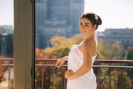 Portrait of sexy lady in bath towel standing on the balcony. Sun rays fall on elegant womanの写真素材