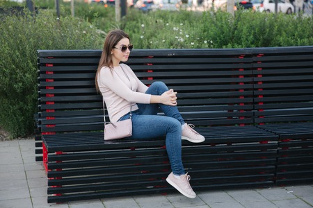 Beautiful girl sitting on the bench in centre of the city. Big banch outsideの写真素材