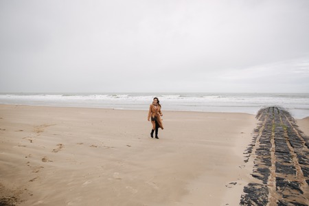 Happy woman walkin on the beach along the North Sea. Outside is cold and rainyの写真素材