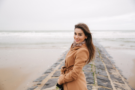 Portrait of beautiful woman walkink along the coast near the north sea. Elegant lady in brown coat with fashion make up stand in front of the seaの写真素材