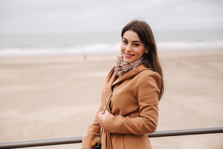 Stylish lady with make up in beautiful coat standing along North Sea. Woman smileの写真素材