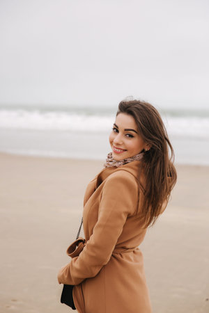 Portrait of beautiful woman walkink along the coast near the north sea. Elegant lady in brown coat...