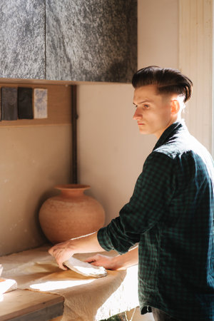 Male potter works with ceramic at his workshop. Handsome young man work inside