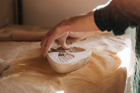 Hands of potter fill the form with a ceramic in the shape of a butterfly. Close up of hands