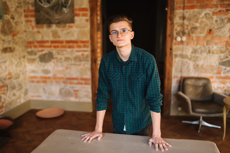 Young man in green shirt in workshop stand by the tableの写真素材