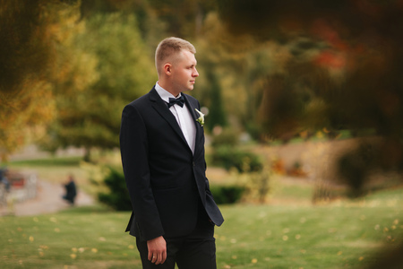 Handsome man in black suit standing outside in autumn. Groom waiting for brideの写真素材