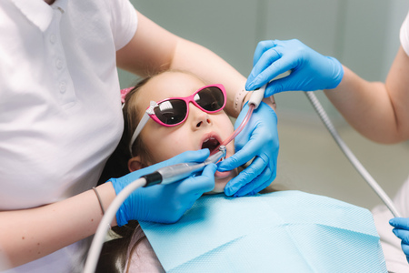 Close up of Little girl in 3D glasses sitting on destal chair at the office and have yearly checkup. Dentist with assistantの写真素材