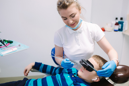 Little boy sitting in dentist in vr glasses and wireless headphones while dentist make x-ray of teeth. male patientの写真素材